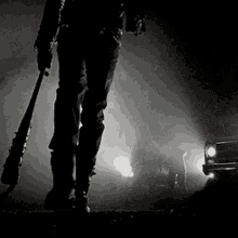 a black and white photo of a person holding a bat in front of a car