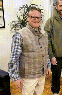 a man wearing a plaid shirt and a vest smiles for the camera