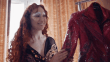 a woman with red hair is smiling while holding a red jacket