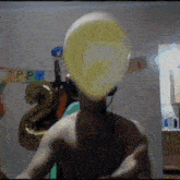 a shirtless man blows up a yellow balloon in front of a birthday banner that says happy