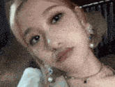 a woman wearing a necklace and earrings is looking at the camera .