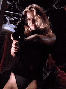 a woman in a black dress is holding a gun in her right hand