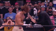a man in a wrestling ring is talking to another man in front of a crowd that is watching a wrestling match .