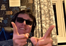 a man wearing sunglasses giving a thumbs up in front of a wall that says level up