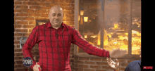 a man in a red plaid shirt is standing in front of a brick wall and a window