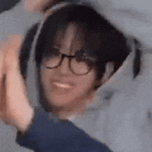 a young man wearing glasses and a hoodie is smiling and waving .