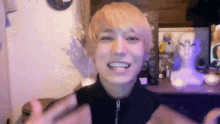 a young man with blonde hair is smiling and waving