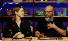 a man and a woman are sitting at a table with a green telephone on the shelf in the background