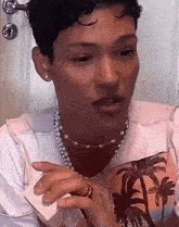 a man wearing a pearl necklace and a ring is talking on a phone .
