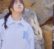 a woman in a white jacket stands next to a rock