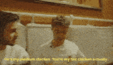 two men are sitting next to each other in a restaurant and one of them is eating chicken .