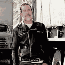 a man wearing a black leather jacket is standing in front of a truck .