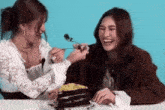 two women are sitting at a table eating a piece of cake together .
