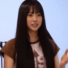 a woman with long black hair and bangs is wearing a brown shirt and standing in front of a microphone .