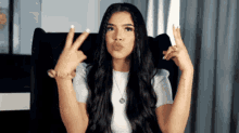 a woman with long hair is sitting in a chair making a peace sign with her hands