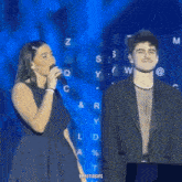 a woman singing into a microphone next to a man with a keyboard in the background with the letters z and w visible