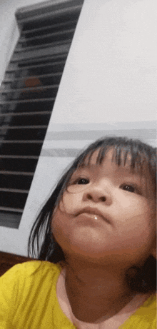 a little girl in a yellow shirt is looking up at the camera .