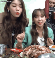 two girls are sitting at a table with a plate of food in front of them
