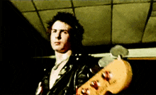 a man in a leather jacket holds a guitar