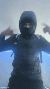 a man wearing a mask and a hooded jacket is giving a thumbs up sign