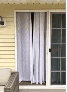 a sliding glass door with a white curtain on it is open to a porch .