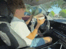a man is sitting in the driver 's seat of a car eating a hamburger .