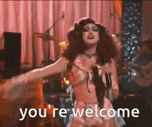 a woman in a drag queen costume is dancing on a stage and says you 're welcome .