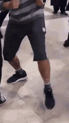 a man in a striped shirt and shorts is dancing on a tile floor .