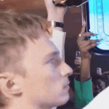 a man in a green shirt is looking at a screen while holding a cell phone .