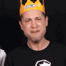 a man wearing a yellow crown and a black shirt is making a funny face .