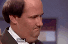 a bald man in a suit and bow tie is making a face .