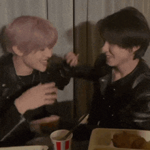 a couple of men are sitting at a table eating chicken and drinking a cup of sauce .