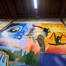 a man is doing a trick in front of a colorful mural with the letter m on it