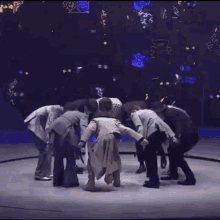 a group of people are standing in a circle on a stage with neon lights in the background .