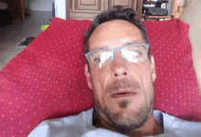 a man with glasses is laying on a red pillow .