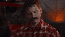 a man with a mustache is wearing a plaid shirt