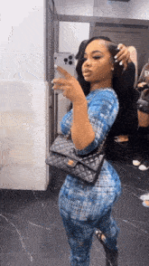 a woman in a blue jumpsuit is taking a picture of herself in a bathroom mirror .