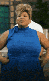 a woman in a blue dress is standing with her hands on her hips and looking at the camera .