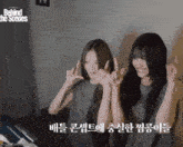 two girls are sitting next to each other in a room and making funny faces with their hands .