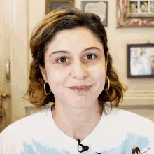 a woman wearing hoop earrings and a tie dye shirt smiles at the camera