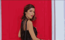 a woman in a black top is standing in front of a red door .