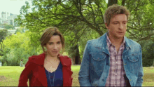 a man and a woman are standing in a park with trees in the background