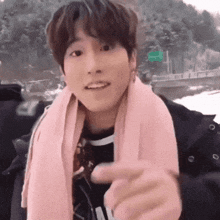 a young man wearing a pink scarf around his neck points at something