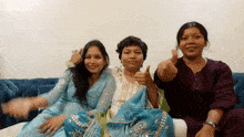 three women sitting on a blue couch giving thumbs up