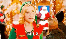 a woman dressed as an elf is standing in front of a christmas tree and looking at the camera .