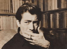 a man is covering his mouth with his hand in front of a bookshelf