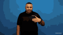 a man in a black shirt is covering his eyes with his hand while standing in front of a blue backdrop