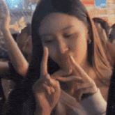 a woman is making a peace sign with her hands in front of her mouth .