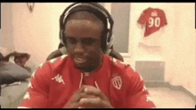 a man wearing headphones and a red shirt is sitting in a room with a jersey on the wall .