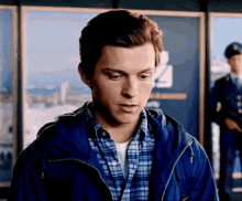 a man in a blue jacket and plaid shirt is standing in front of a wall with a picture of a city on it .